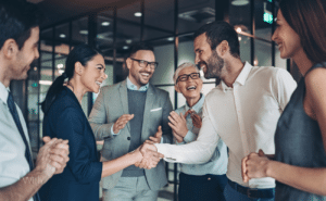 A group of co workers in an office. Two of them are shaking hands.