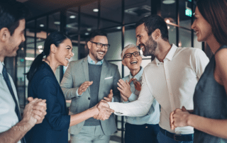 A group of co workers in an office. Two of them are shaking hands.
