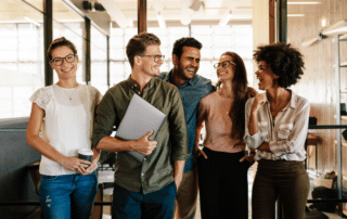 5 teammates standing in an office, they are all smiling and laughing.