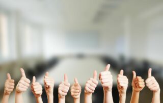Many hands with thumbs up with an office background.