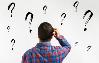 Male with a hand on his head, doubtful and surrounded by question marks.