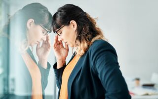 A woman looking concerned with a hand on her head and her image being reflected.