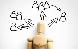 A humanlike figurine over a piece of paper with a drawing of a few groups of people forming from it.